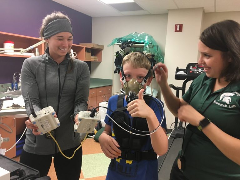 kid trying on an oxygen mask with two research students holding the mechanics of the mask