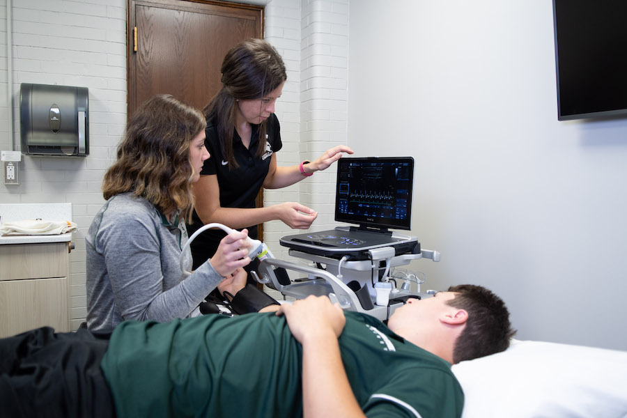 two women looking at a monitor with someone laying on a clinical bed