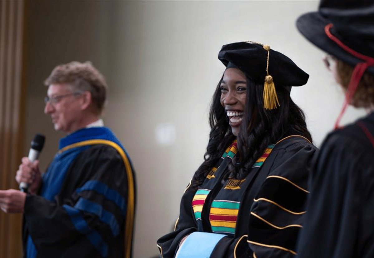 Doctoral degree candidate dressed in regalia, smiling on stage