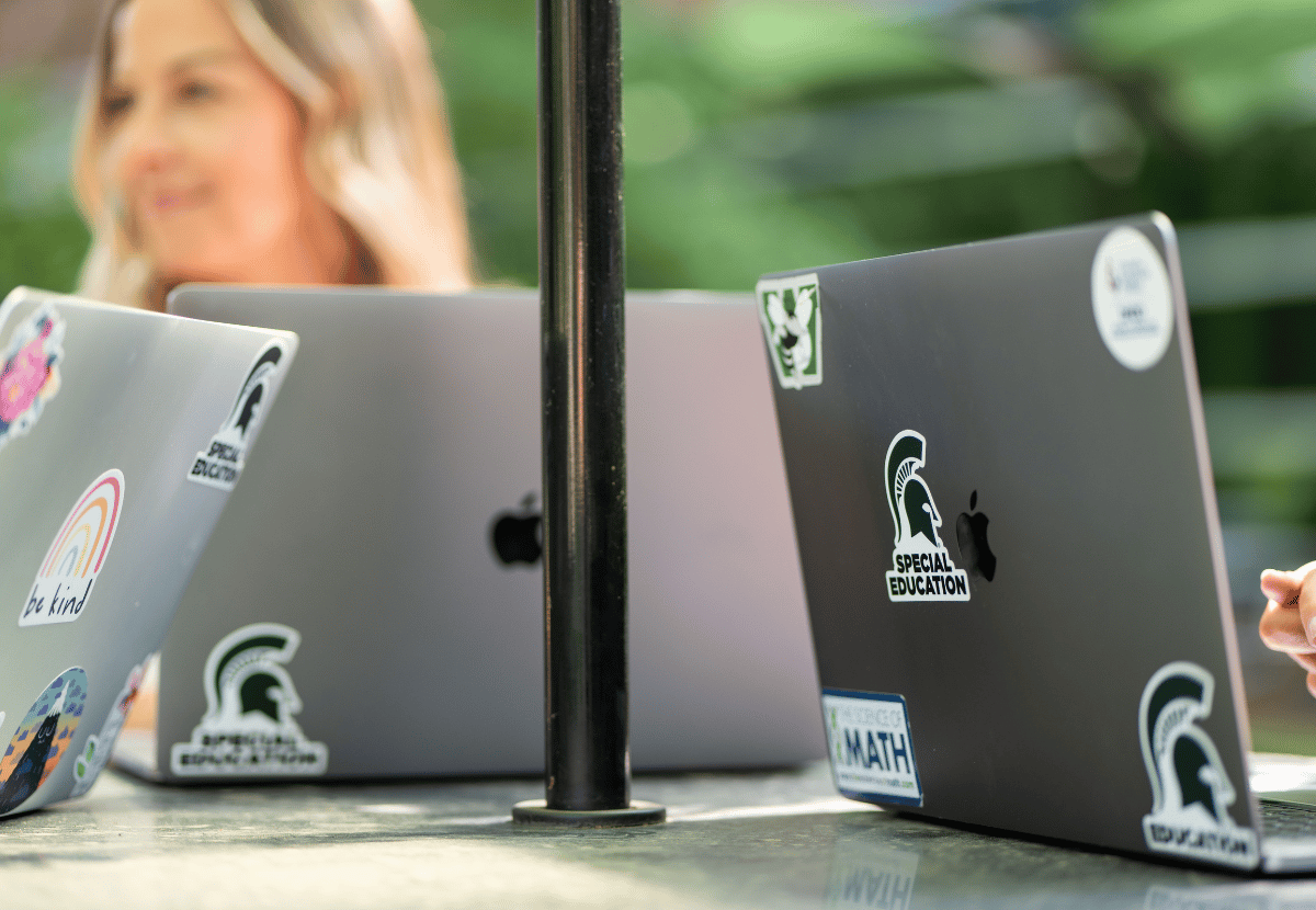 Laptops open on a table with stickers on them. The stickers, green Spartan helmets with "Special Education" written below it, are in focus.