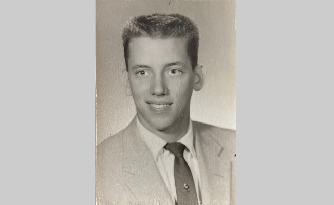 A black-and-white portrait of a young William Schmidt, dressed in a suit and tie, with neatly combed hair. He appears to be in his late teens or early twenties, looking confidently at the camera.