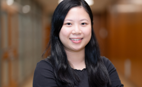 Headshot for Ming Ming Cheung. Cheung smiles toward the camera while in a long hallway in Erickson Hall, home to the MSU College of Education. Cheung wears a black shirt. Cheung's black falls past the shoulders.