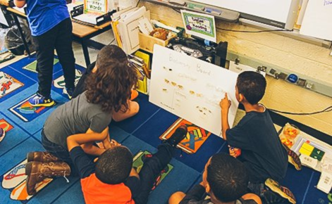 Students gather around a board to work on a science project