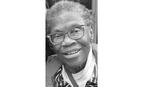 Joyce Grant photo in black and white. Joyce wears a turtleneck and striped blouse. Joyce wears dark-rimmed glasses. Joyce's hair is curly, white and cropped close to the head.