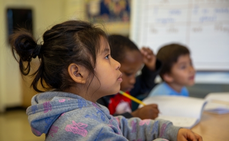 A young girl studies intently in a classroom.