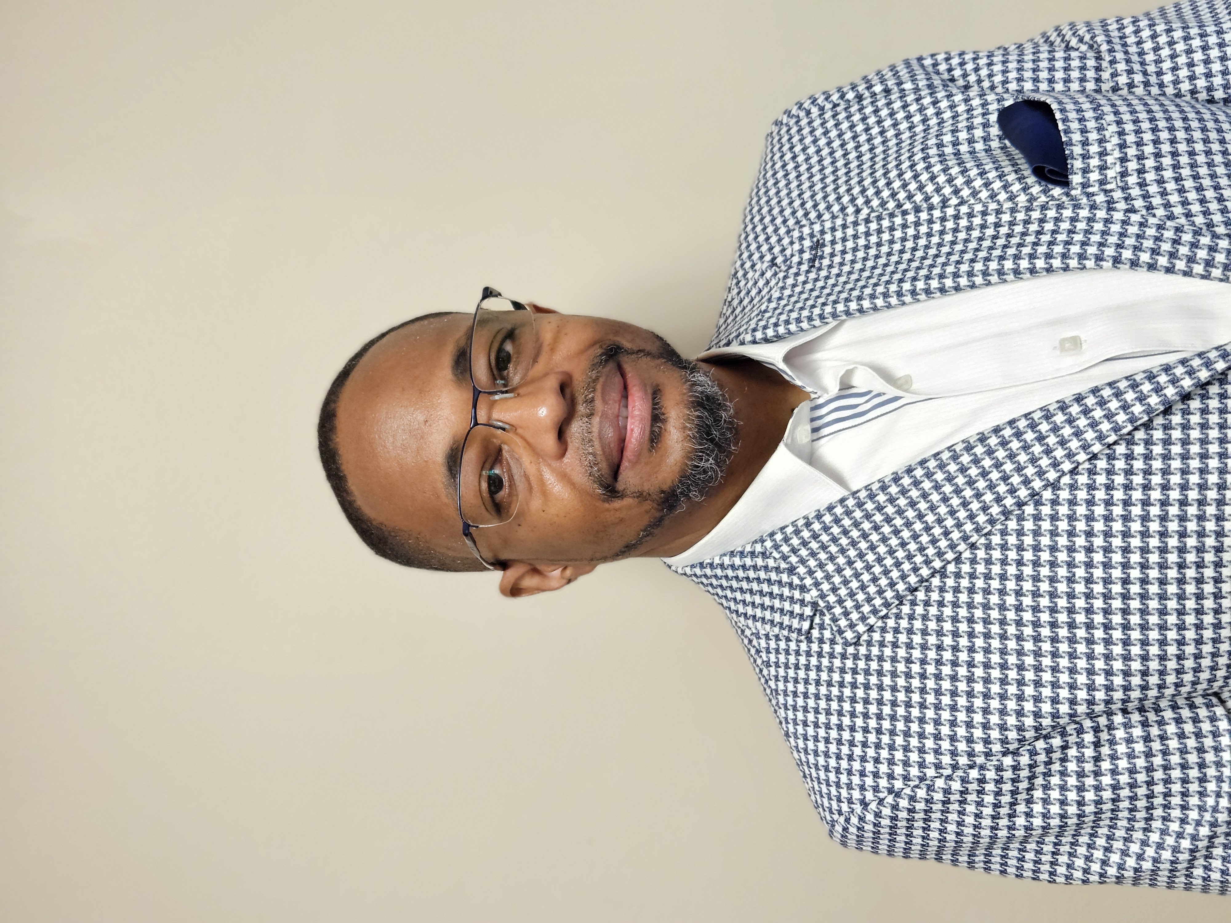 Theodore Ransaw headshot. Ransaw wears a blue and white checkered blazer over a white button down shirt.