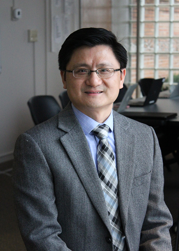 Kui Xie smiles toward the camera in a conference room. Xie wears a gray suit and wire-rimmed glasses.