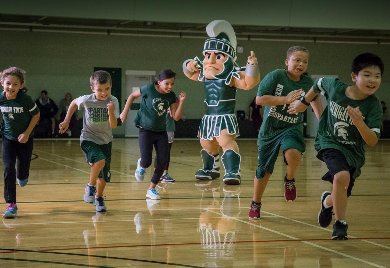 sparty running with kids in a gym