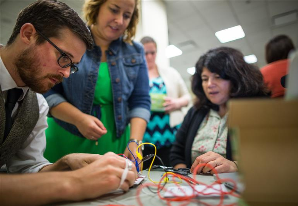 Three people gathered around a table, working with a circut board and wires