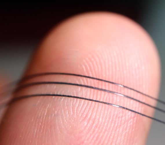 close up of a finger holding Three flexible NeuroString sensors.
