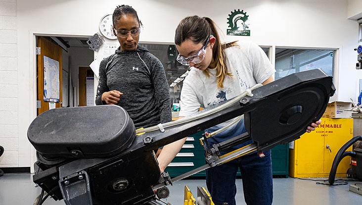 Students working on a heavy cutting machine in a Women's Workshop