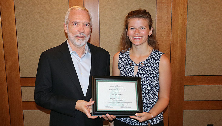 Student stands with Von Ehr while holding a scholarship certificate.