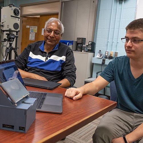 Anil Jain, MSU Professor of Biometrics Engineering, and their Graduate Students sitting at a table looking a a laptop that has a program for the finger print Raspireader,