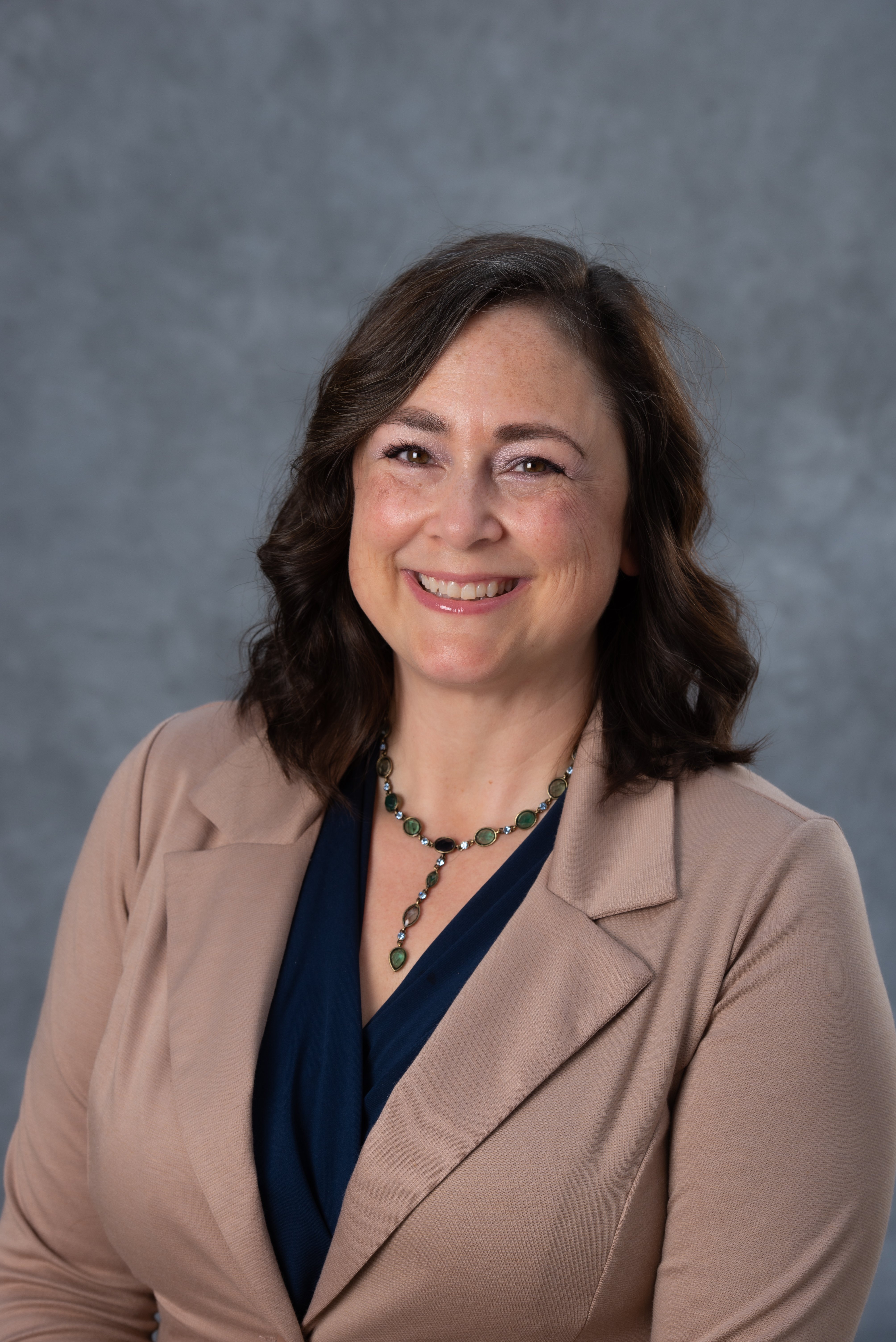 A brunette women dressed professionally smiling in front of a gray backdrop