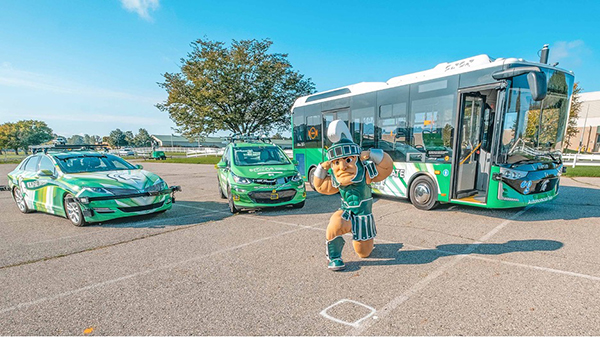 Sparty poses with MSU’s two autonomous cars and its autonomous bus. Credit: Derrick L. Turner