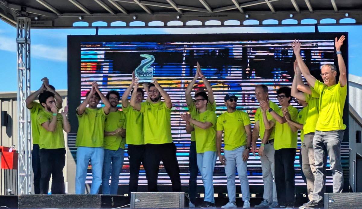 Group of people wearing bright green t-shirts on a stage holding up a first-place trophy.