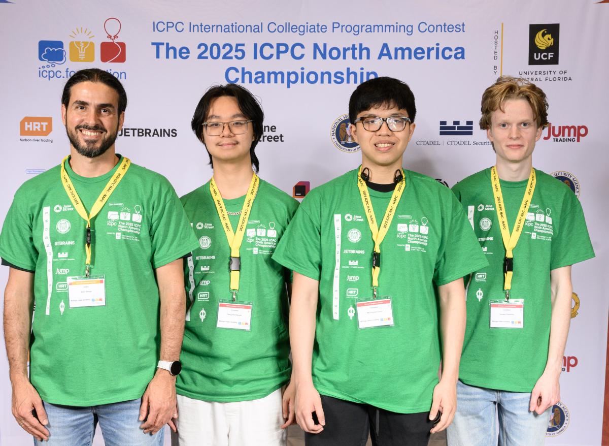 Four students in green t-shirts smiling for the camera in front of a sign that reads 'The 2025 ICPC North America Championship'
