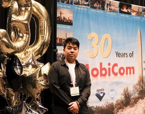 Yimeng Liu stands by ?30 Years of MobiCom? banner and gold balloons at 2024 event in Washington, D.C.