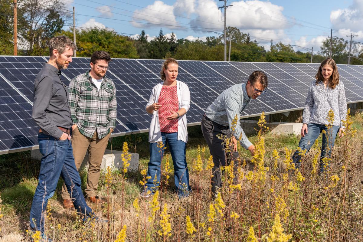 Group of five people standing infant of a solar array in a field.