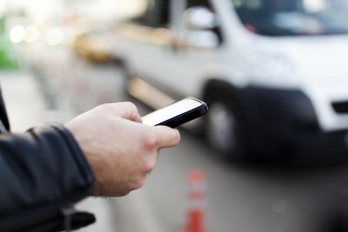 Person holding smart phone in front of vehicle