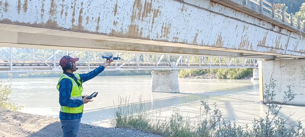 Surya Congress stands in front of a white metal bridge with a drone.