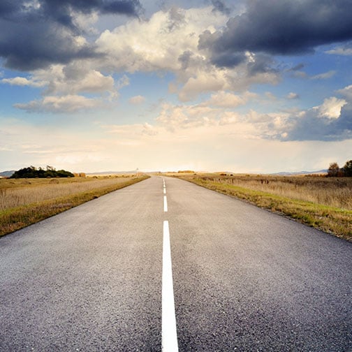 a cloudy sunny shot of a road going in the horizon