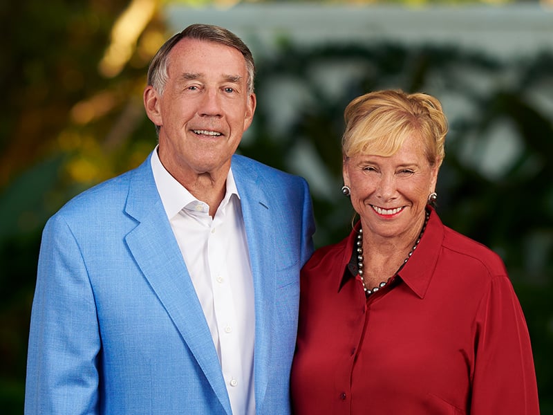 Larry Leinweber and Claudia Babiarz stand together outdoors, dressed in formal clothing with greenery in the background.