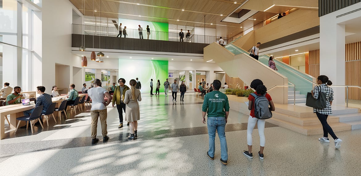 Bright lobby with seating, green accent wall, and central staircase; people gathered and walking.
