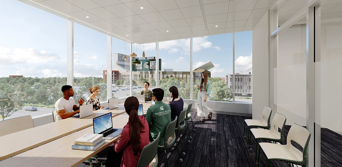 Meeting room with large windows, people seated around a table with laptops, and campus view outside.