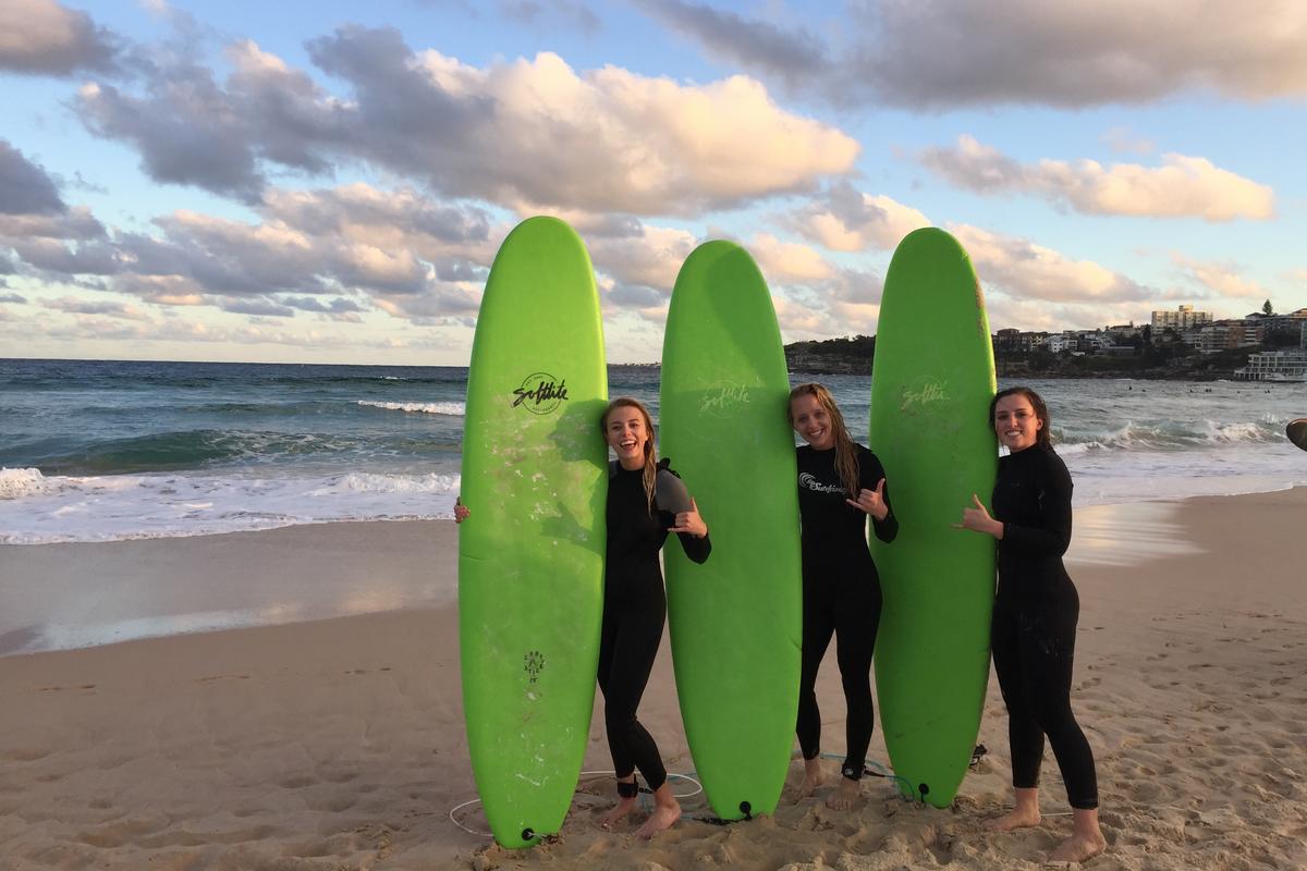 Three women stand with surf boards on the beach.
