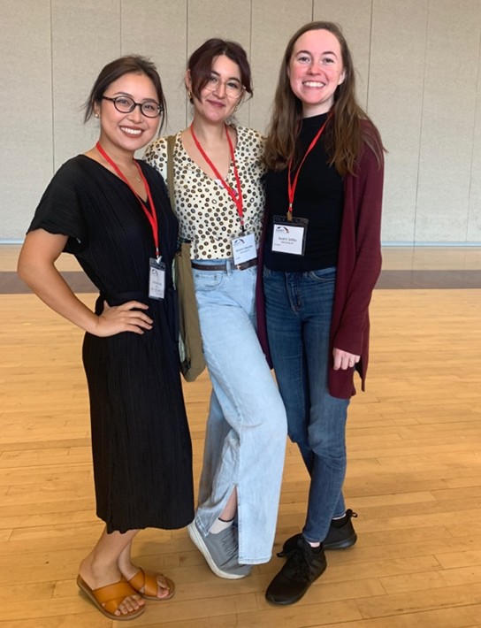 Three graduate students smile with their arms around each other.
