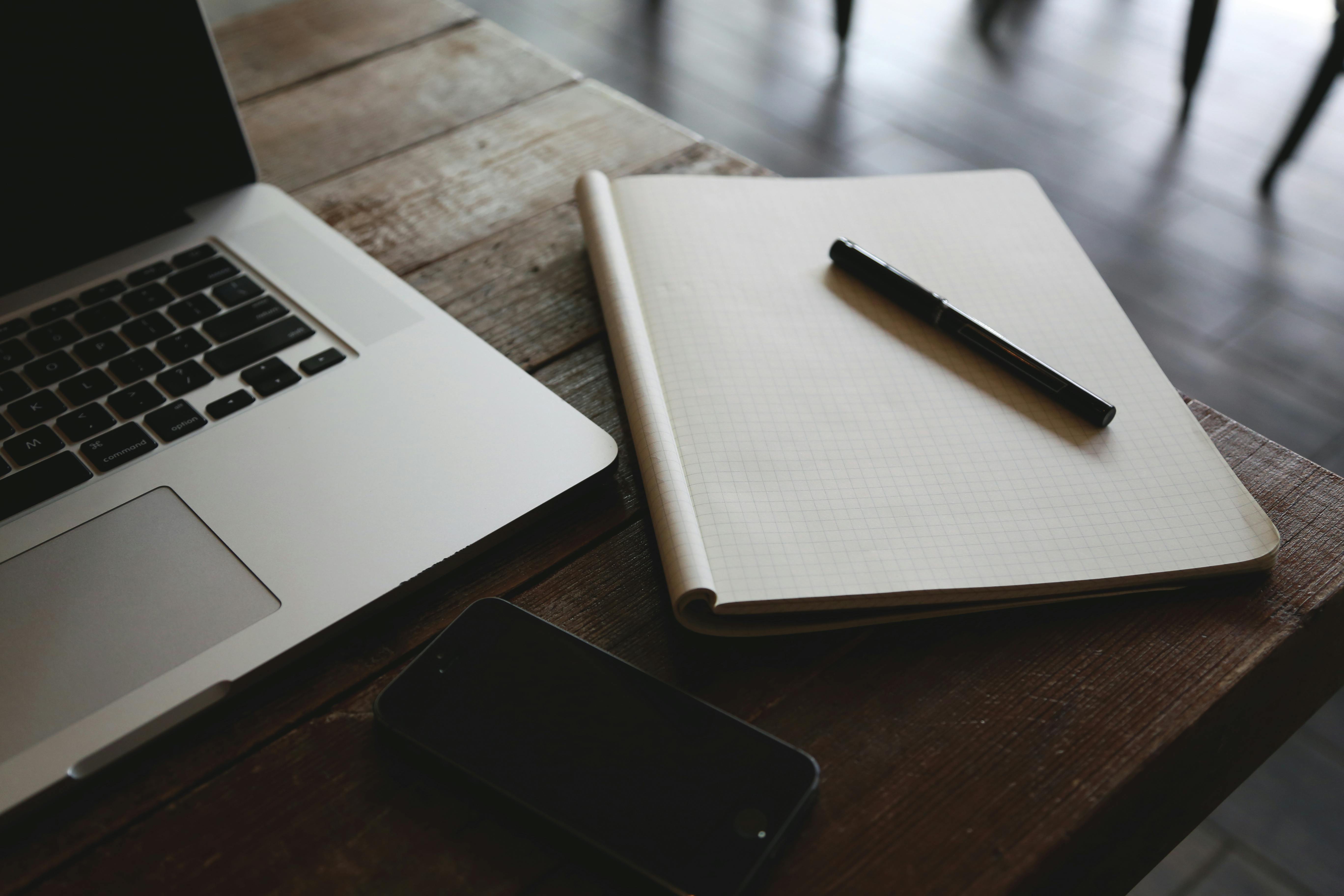 A notebook and pen next to a computer on a table.