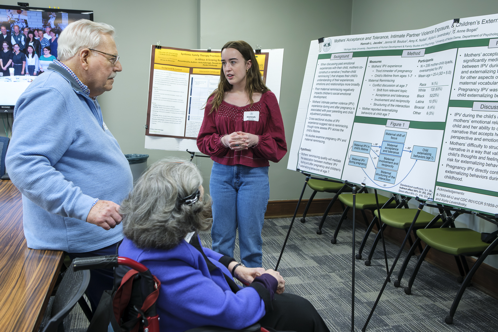 Graduate student speaks with two elderly former faculty with research posters in the background.