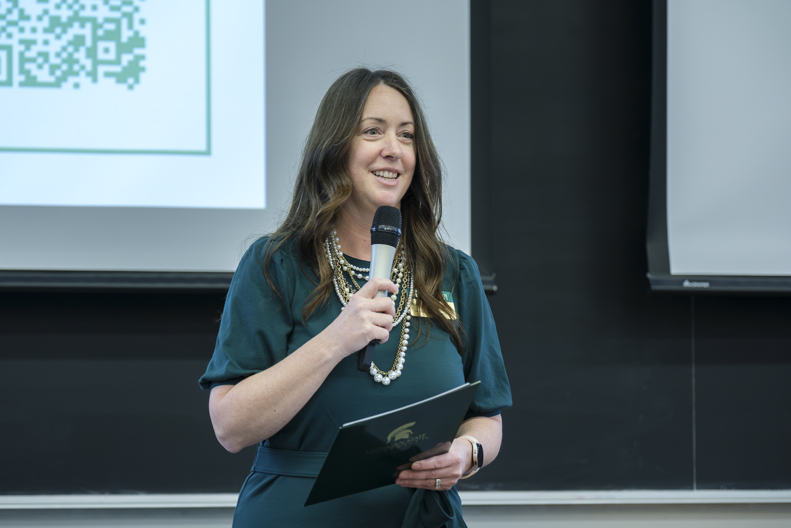 Woman speaks to a room of people through a microphone.