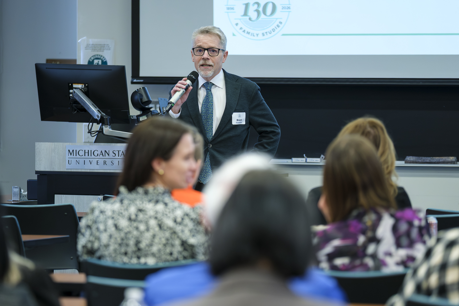 Man speaks through a microphone to a room of people.