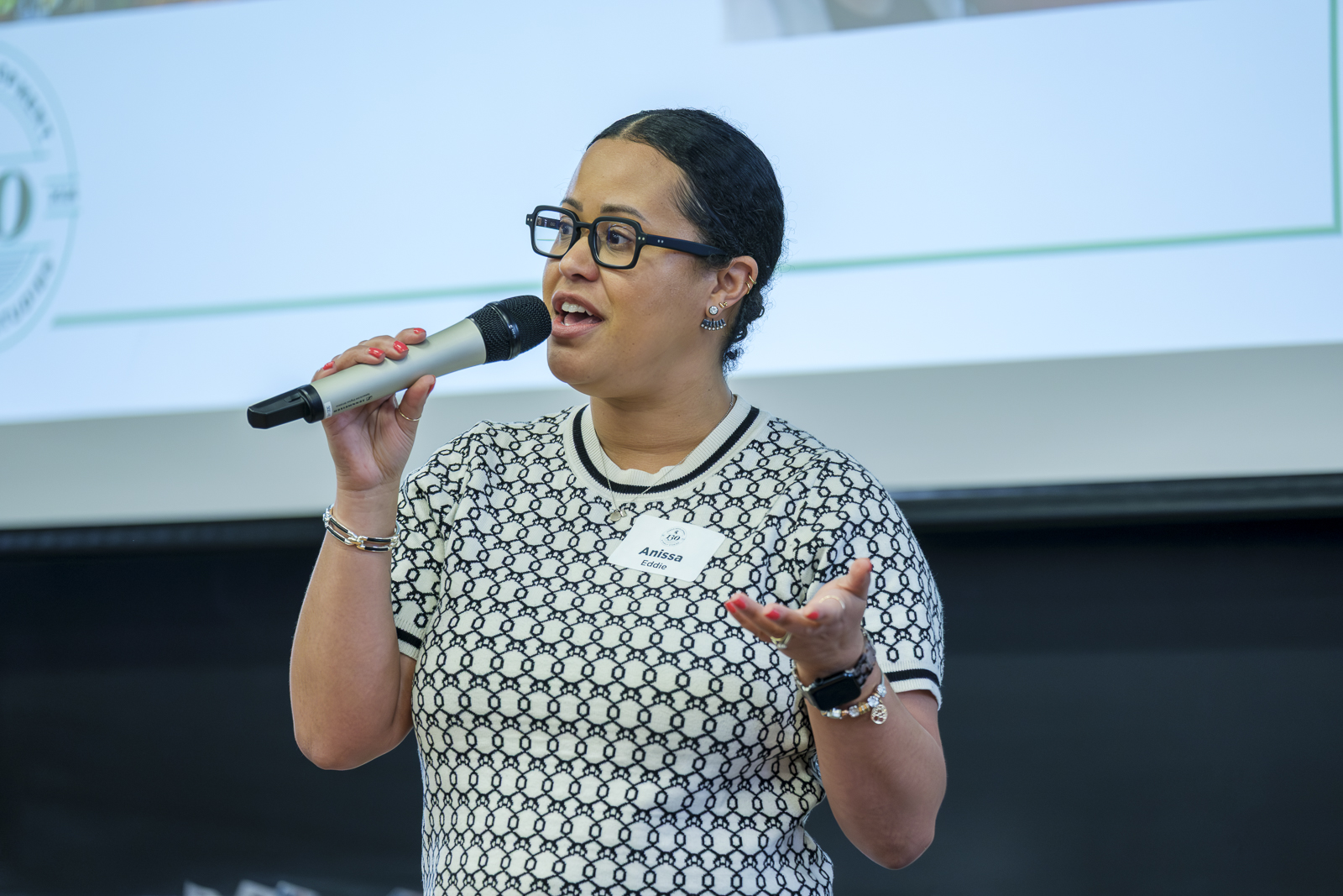Woman speaks into a microphone to a room of people.