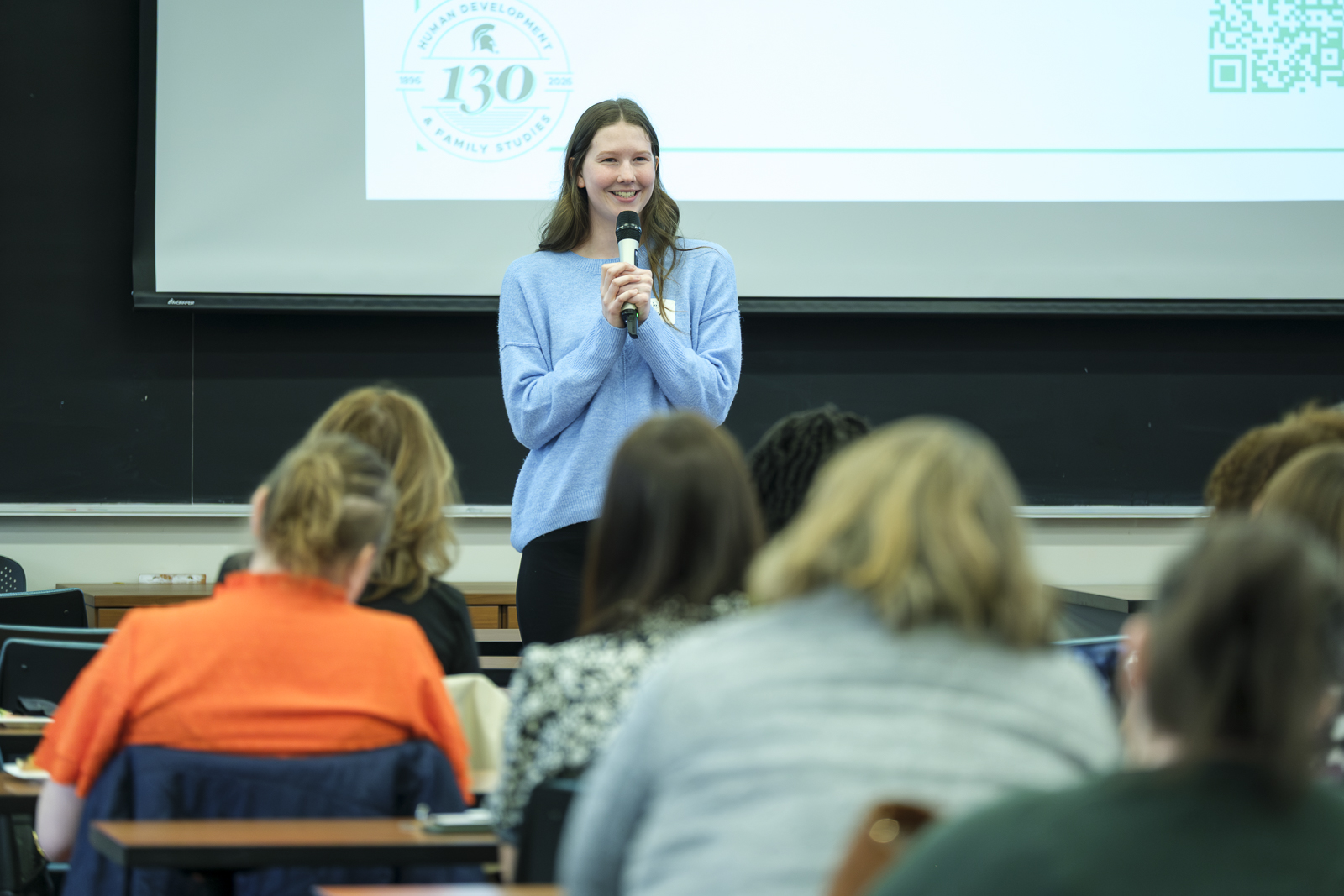 Woman speaks to room of people through a microphone.