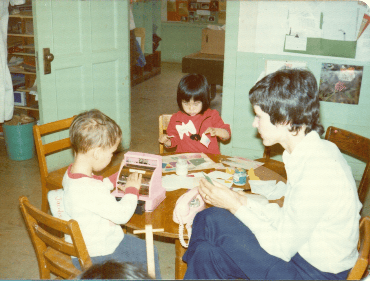 Teacher and children sitting at a table with toys.