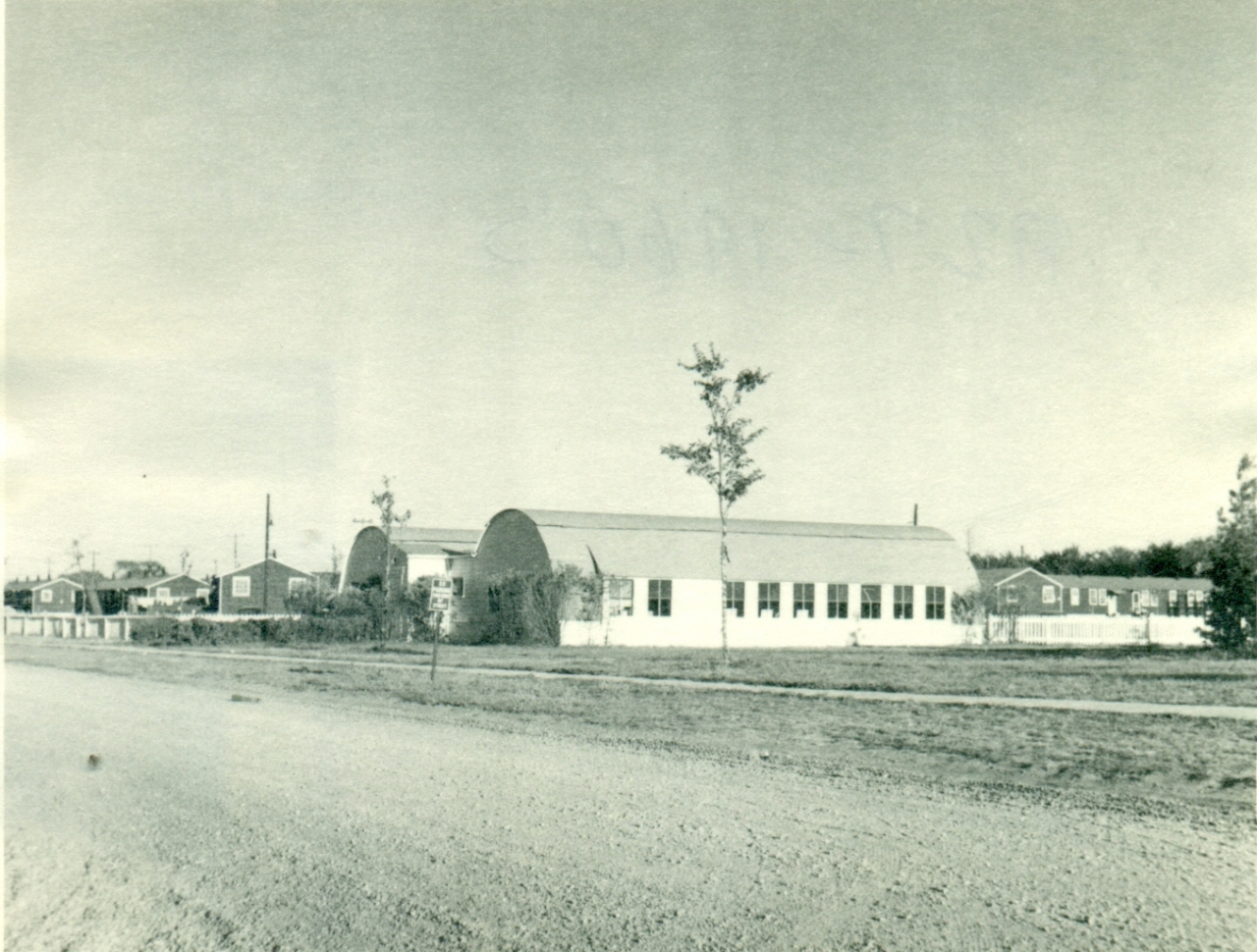 Quonset huts with houses in the background.