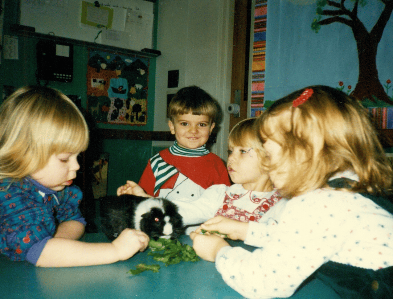 Four children at table petting guinea pig.