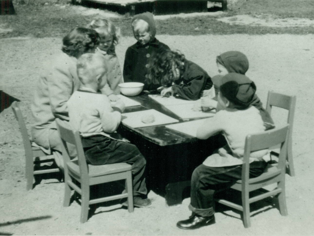 Children sitting at a table outside coloring.