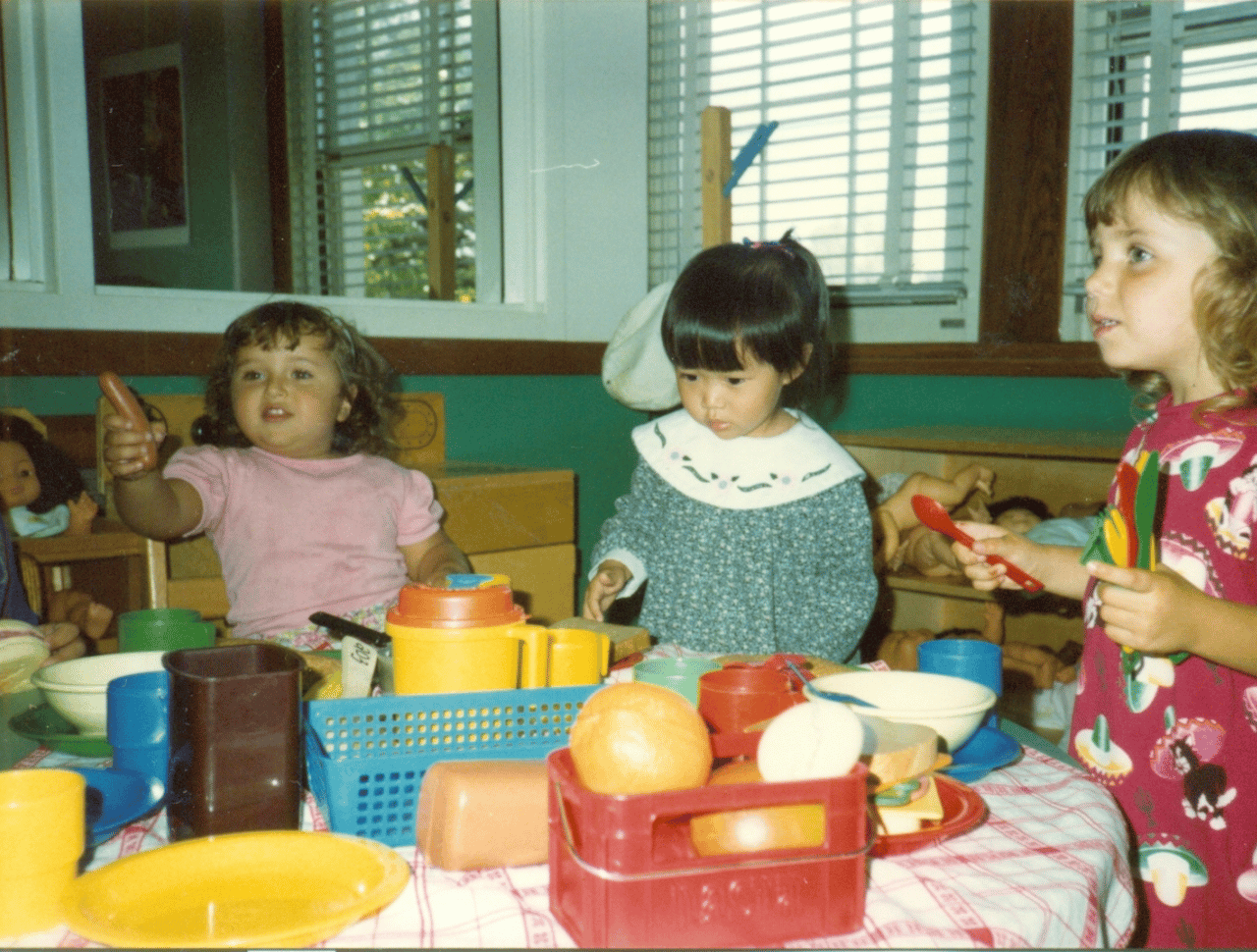 Three kids at table playing with plastic food toys.