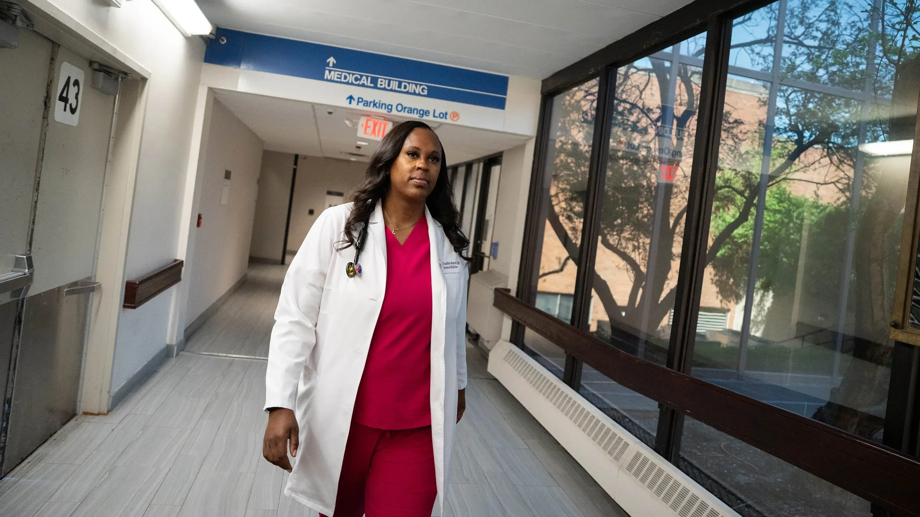 Standifer-Barrett wearing her white coat and a pink scrubs while walking down a hospital hall.