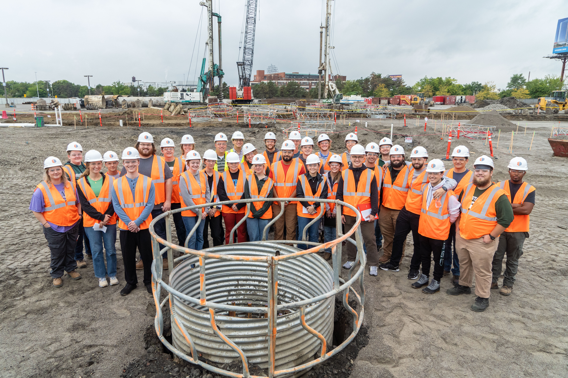 MSU Egineering students and faculty wearing construction hats posing on the Henry Ford + MSU Research Center construciton site.