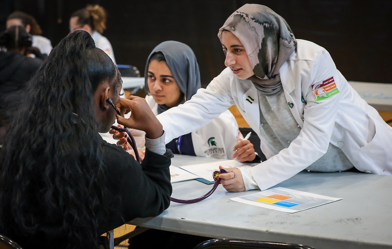 MSU CHM medical student helping a high school student use a stethoscope.