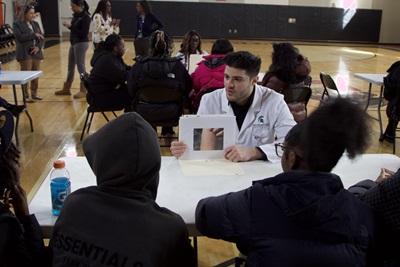 MSU medical student showing a case study to to high school students at a table.