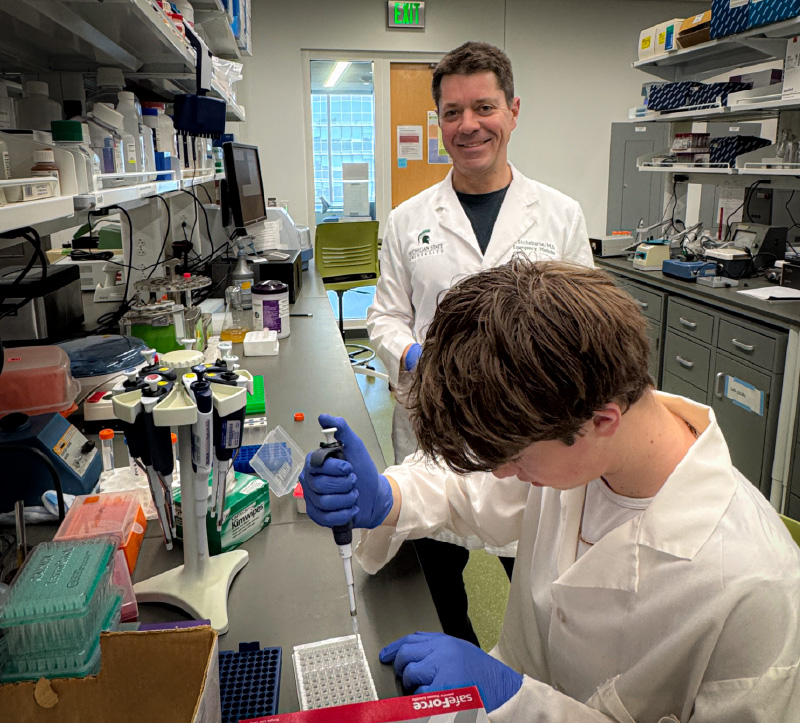 Two people in front of a lab work bench holding a lab tube.