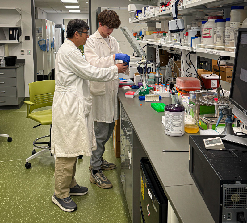 Two people standing in front of a lab work station.