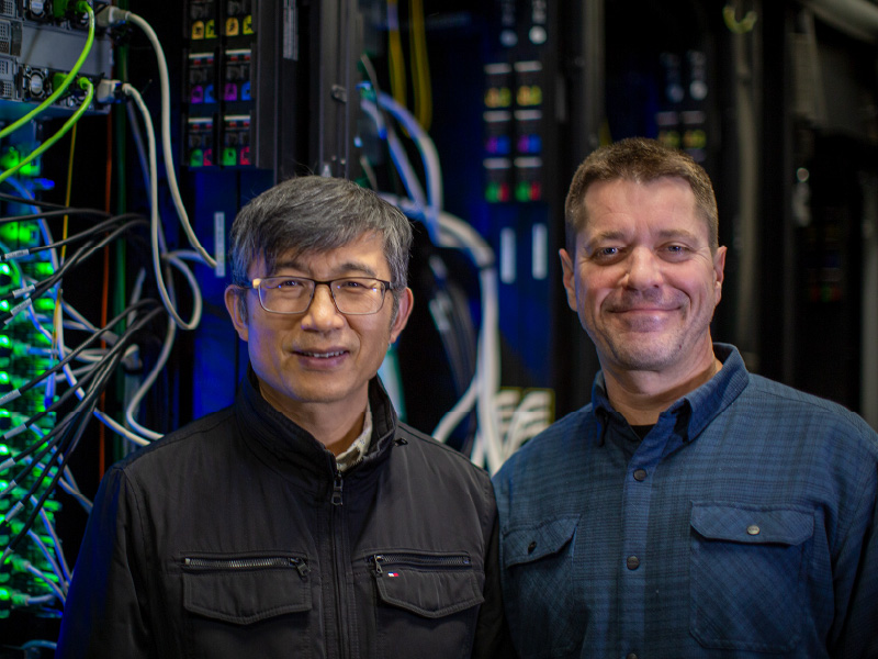Brett Etchebarne and Zenggang Li standing in front of green and blue lights and wires.