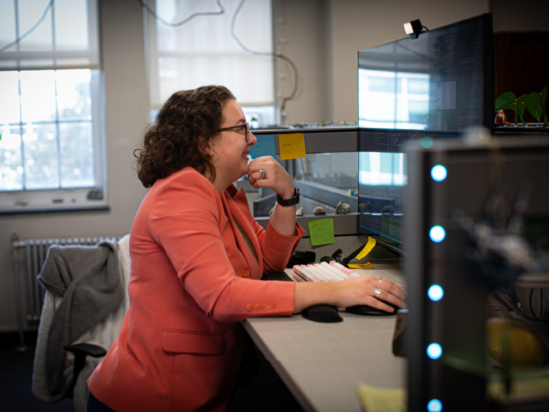 Heidi Krauss sits at her workstation with a large monitor displaying computer code. 